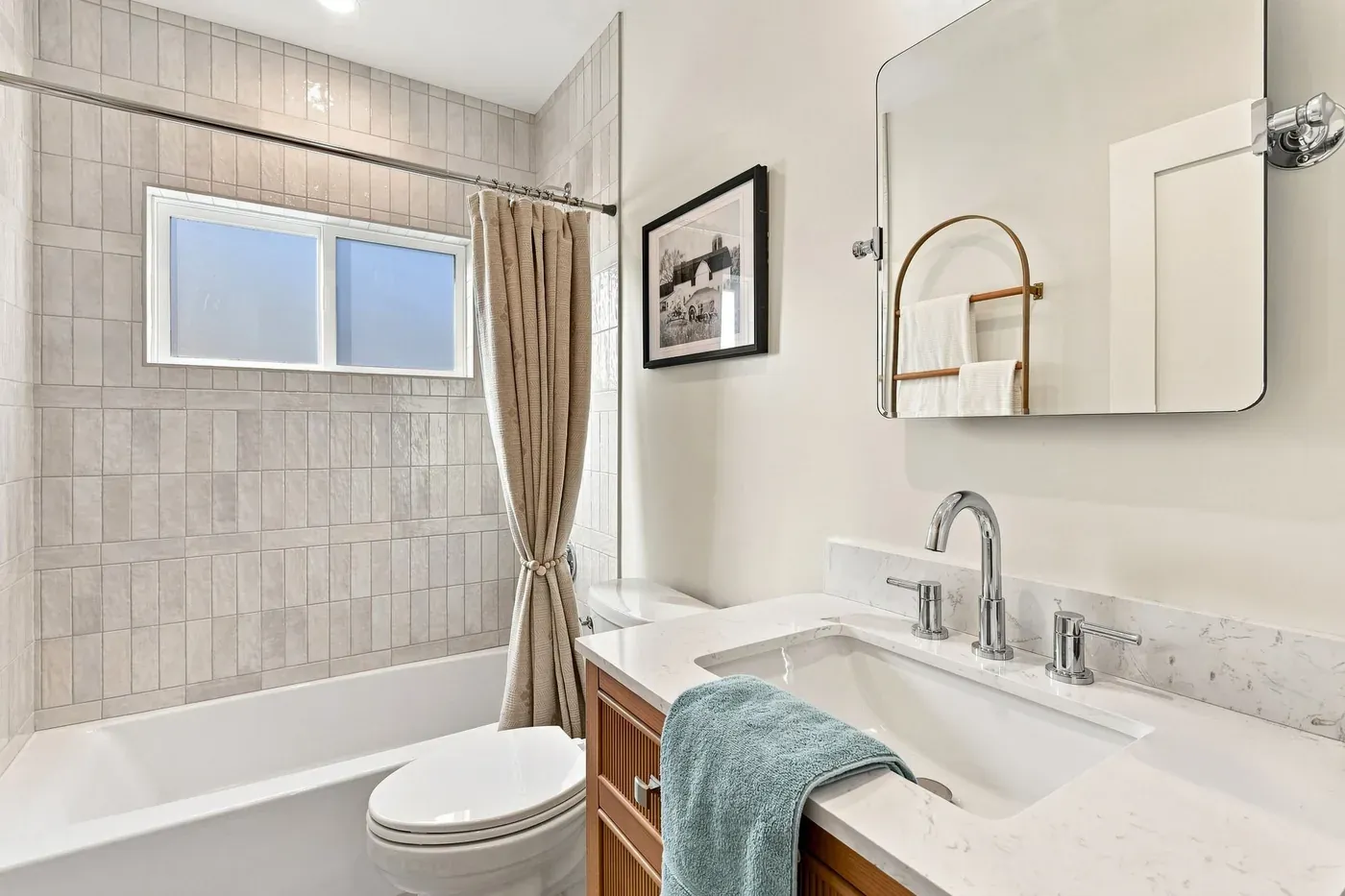 Bathroom with a tiled tub surround, wood vanity, and white stone countertop