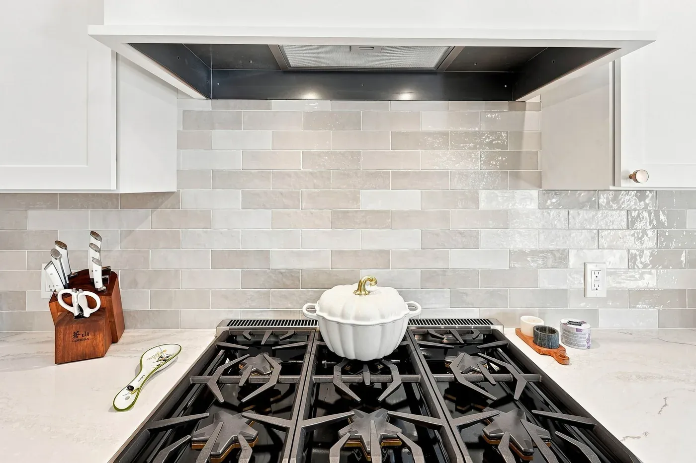 Gas range set against a glazed subway-tile backsplash beneath a white range hood