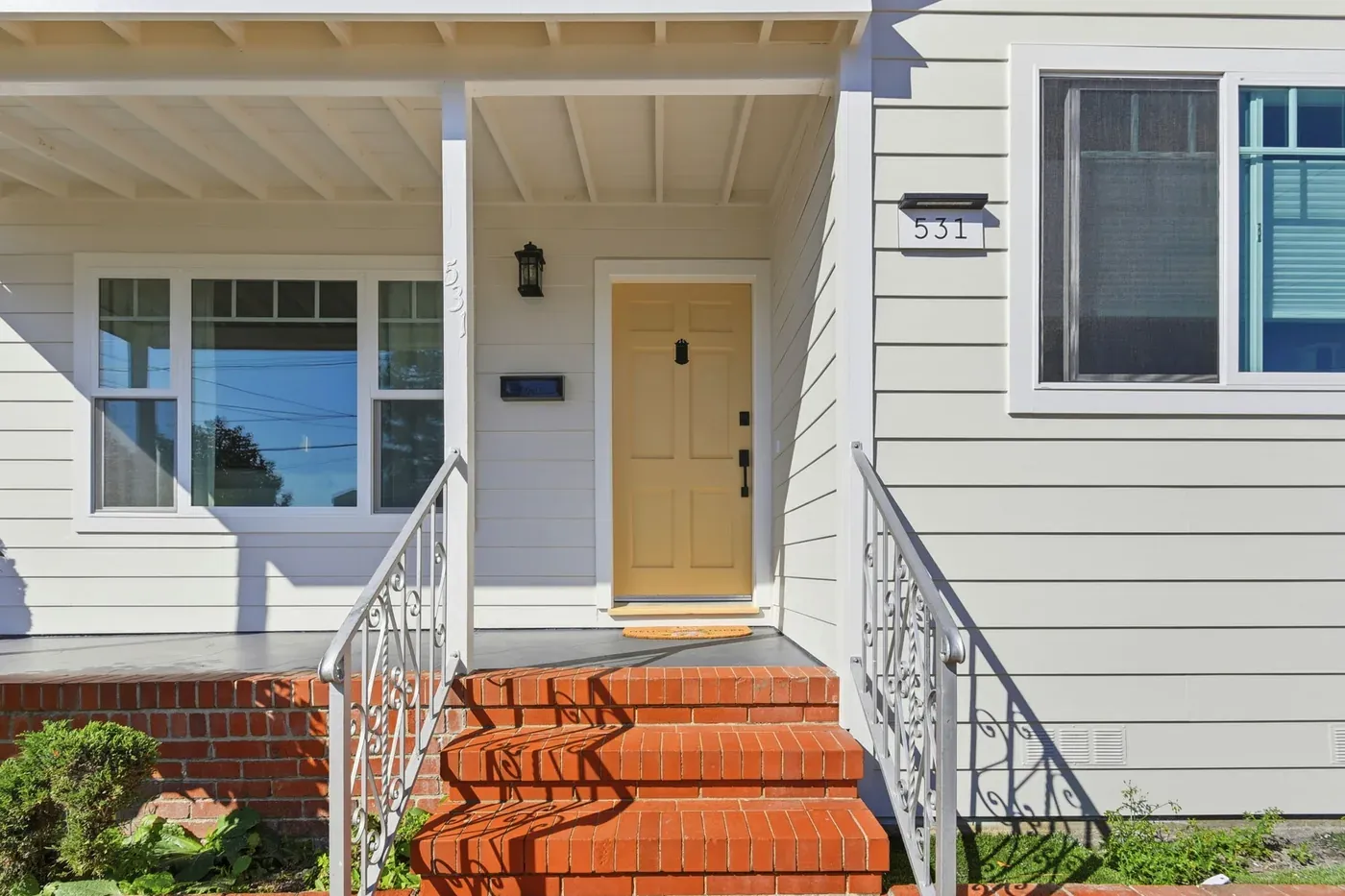 Covered front porch with brick steps, white wrought-iron railings, and a yellow front door