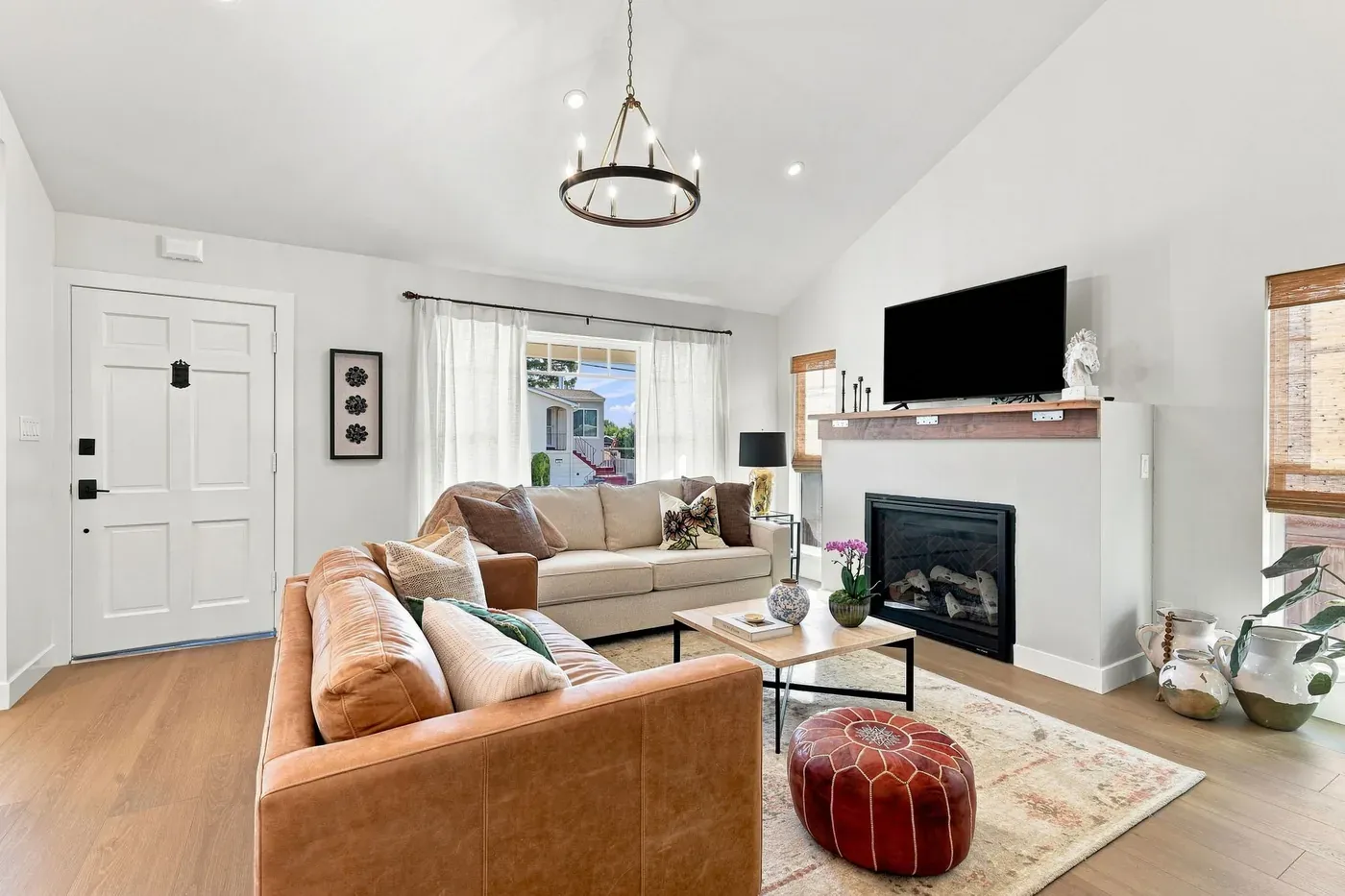 Living room under a vaulted ceiling with a ring chandelier, leather sofas, and a gas fireplace, seen from the front door