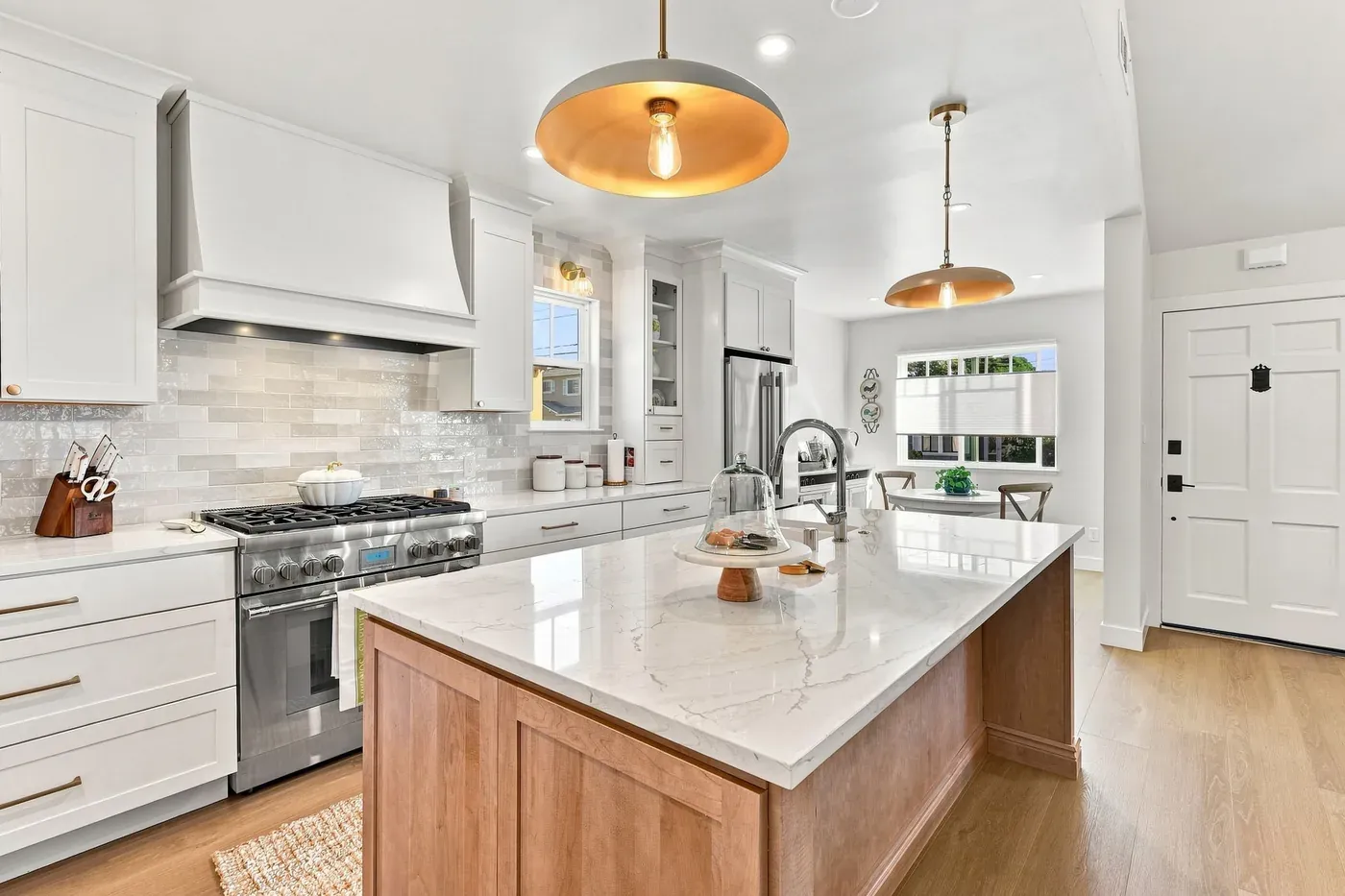 Kitchen with a wood island topped in white stone, white shaker cabinets, a hooded gas range, and brass dome pendant lights