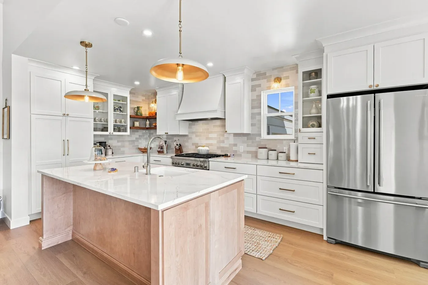 Kitchen seen from the dining side, showing the island sink, glass-front cabinets, and stainless steel refrigerator